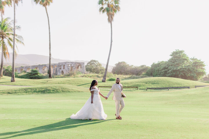 Bride and groom walking across a tropical golf course at a luxury resort during their destination wedding in Punta Cana.