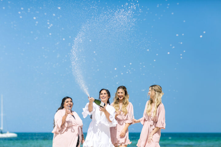 Bride celebrating with her bridesmaids on a Caribbean beach with champagne during a destination wedding in Punta Cana.
